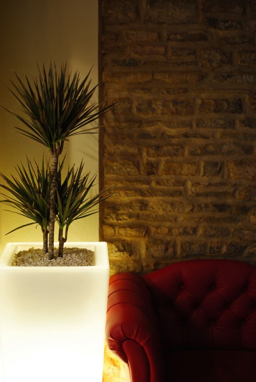 A lit planter beside a red chesterfield and a stone wall
